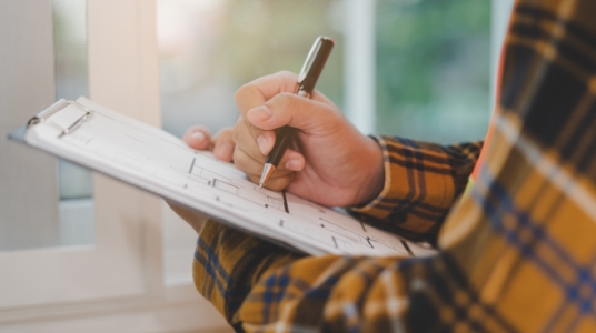A person in a flannel shirt holds a clipboard. 