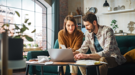A couple looks at a laptop together in a modern apartment living area.