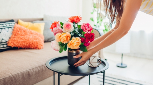 A woman sets a vase of fresh flowers down on a small accent table